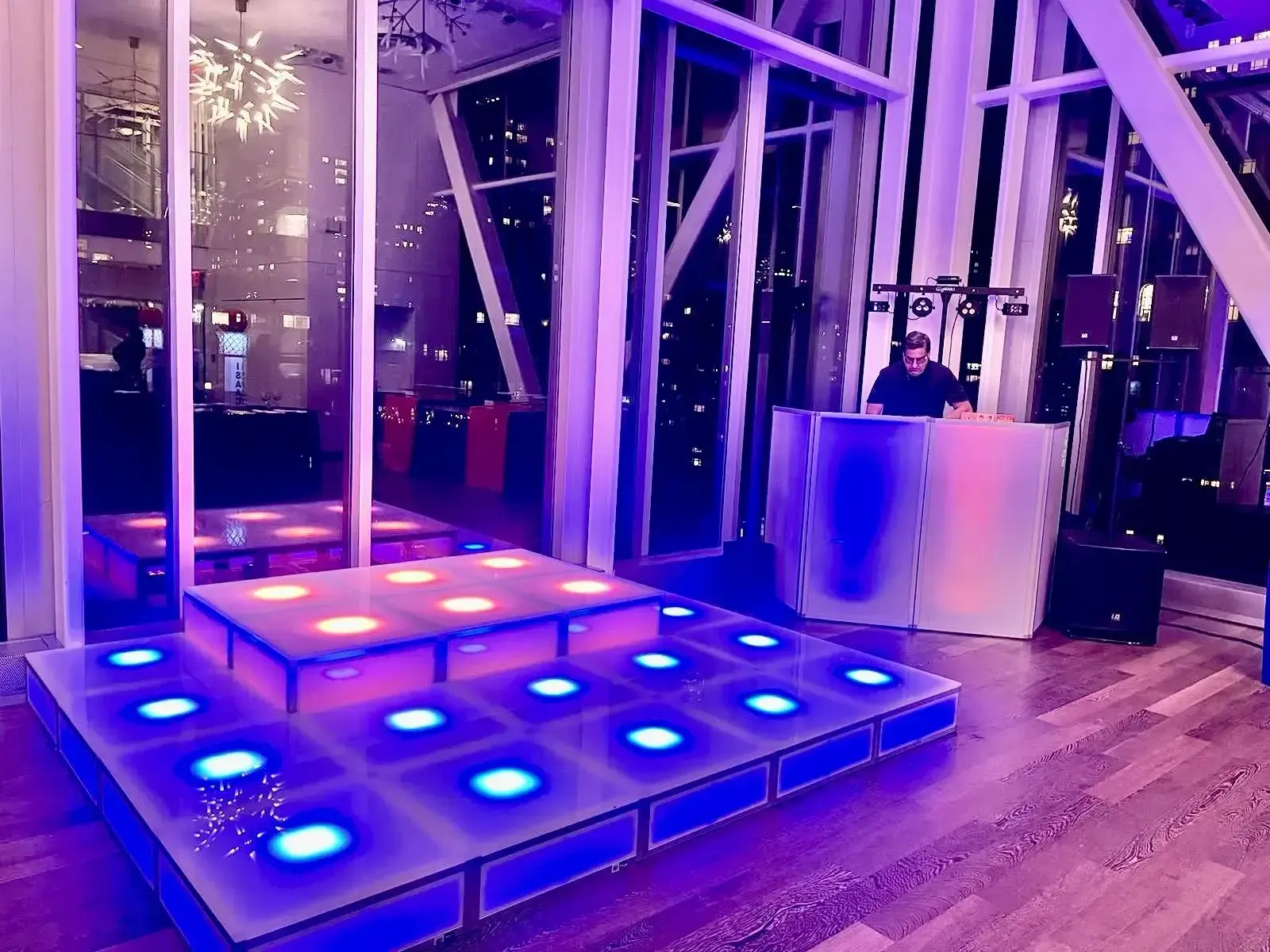 Illuminated LED stage glowing in blue, pink and orange with a DJ booth and the Manhattan skyline through the windows at night